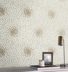 A modern desk is styled with a gold lamp, a framed black-and-white photo of the Eiffel Tower, and stacked books. Behind, York Wallcoverings’ Petite Leaves Wallpaper adds elegance with its gold floral pattern on a light background.