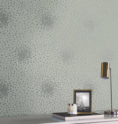 A wall decorated with York Wallcoverings’ Petite Leaves Wallpaper in a gray floral burst pattern on pale green sets the backdrop for a white desk, which displays a gold lamp, a glass candle, and a framed black and white photo of the Eiffel Tower.
