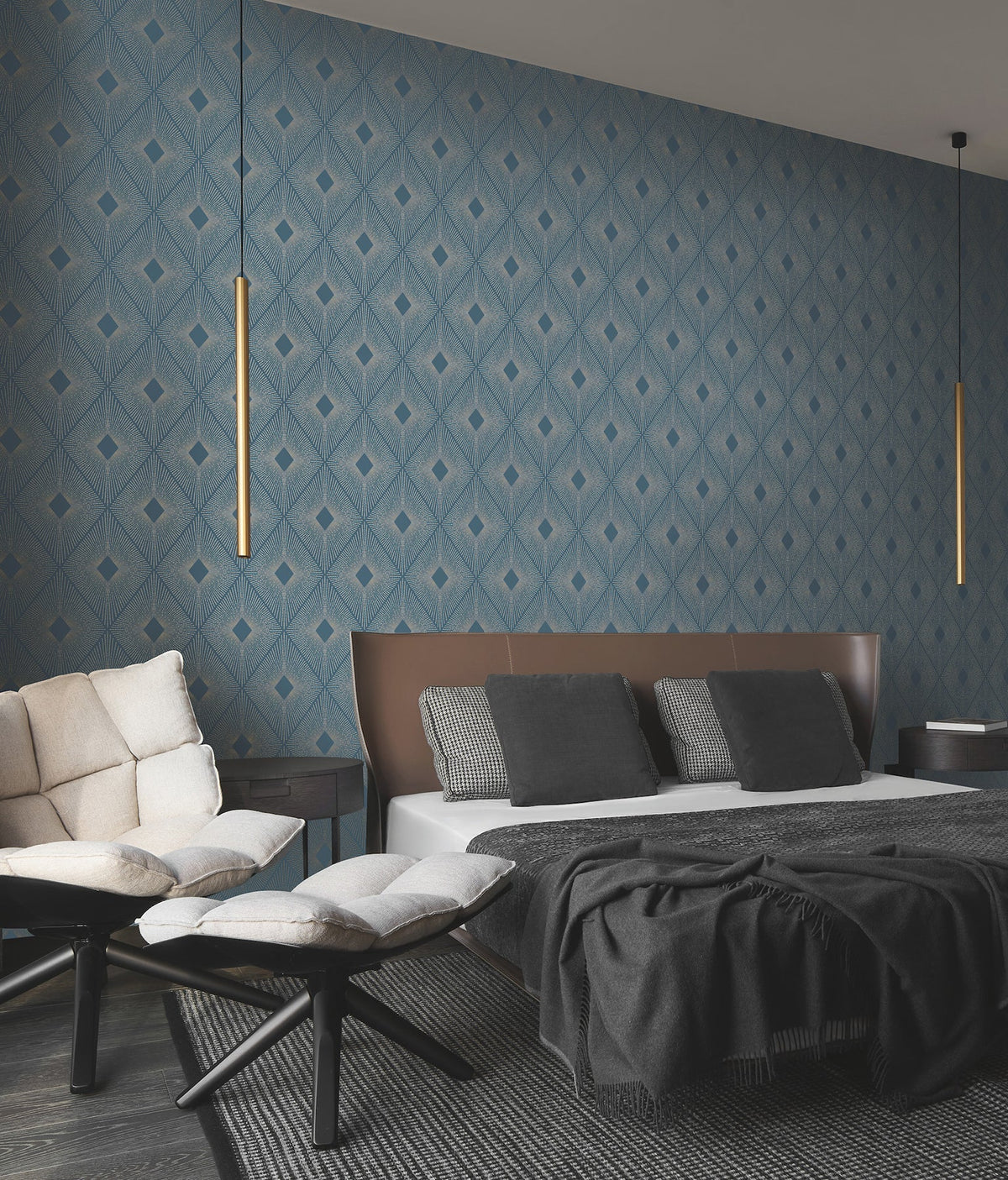 Modern bedroom featuring Harlowe Wallpaper by York Wallcoverings in a geometric blue pattern, a low bed with brown headboard, black and white bedding, cushioned chairs, and two slim pendant lights hanging from the ceiling.