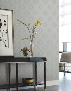 A modern living room featuring a black console table, glass vase with yellow flowers, decorative bowl, framed artwork, and Harlowe Wallpaper by York Wallcoverings in a geometric gray pattern. Sunlight filters through sheer window coverings.