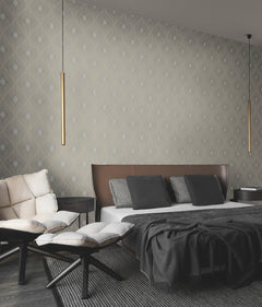 A modern bedroom featuring Harlowe Wallpaper by York Wallcoverings, a bed with dark bedding and gray pillows, two cushioned chairs with ottomans, a side table, and two hanging gold pendant lights.