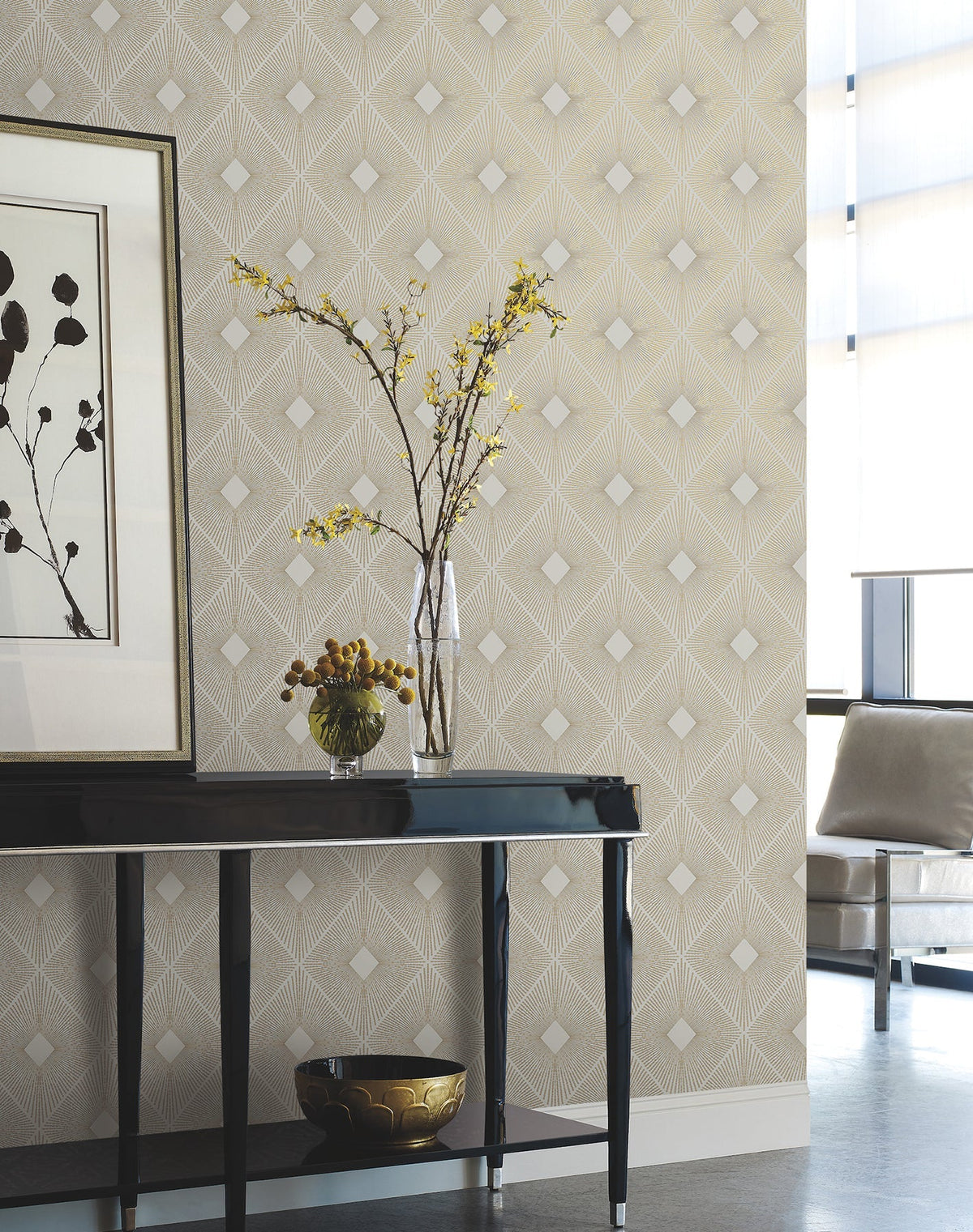 A modern living space featuring Harlowe Wallpaper by York Wallcoverings, complemented by a glossy black console table, vases with yellow flowers, framed artwork, and a beige armchair positioned near large windows with sheer curtains.