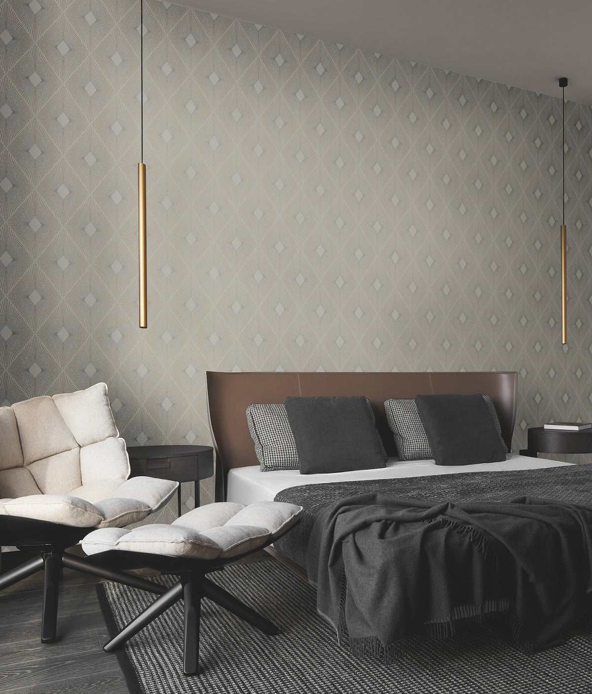 A modern bedroom featuring Harlowe Wallpaper by York Wallcoverings, a brown and white bed with gray pillows, a cream sofa, two footstools, and two slim gold pendant lights hanging from the ceiling.