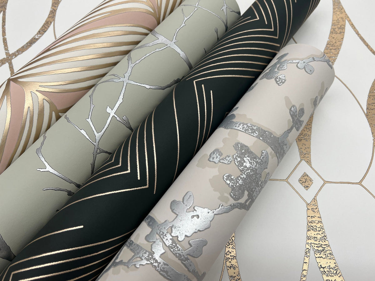 Four rolls of York Wallcoverings’ Shimmering Foliage Wallpaper, featuring metallic gold and silver geometric and floral patterns, are arranged diagonally on a white background with matching gold-accented designs.