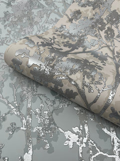 A close-up of York Wallcoverings’ Shimmering Foliage Wallpaper, featuring a metallic silver and beige tree branch pattern on a light gray background.