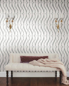 Sure! Here’s your revised sentence incorporating the product data: A tufted cream bench with a mauve pillow and folded throw blanket sits in front of the Graceful Geo Wallpaper by York Wallcoverings. Two brass wall sconces with white lampshades are mounted above the bench, while a dark wooden floor grounds the space.