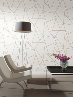 Two modern white chairs, a tall floor lamp, and a black coffee table with a vase of purple flowers sit in a room featuring the Nazca Wallpaper by York Wallcoverings, showcasing a geometric-patterned design in white and gold.