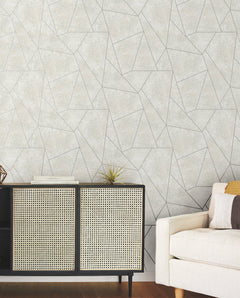 A modern living room features the Nazca Wallpaper by York Wallcoverings in a beige geometric design, paired with a black and cane sideboard displaying books and decor, and a light-colored sofa accented with pillows for a minimal and contemporary atmosphere.