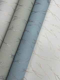 Three rolls of Sprigs Wallpaper by York Wallcoverings in gray, blue, and white, each featuring a delicate linear pattern with metallic accents that resemble thin sprigs or twigs.