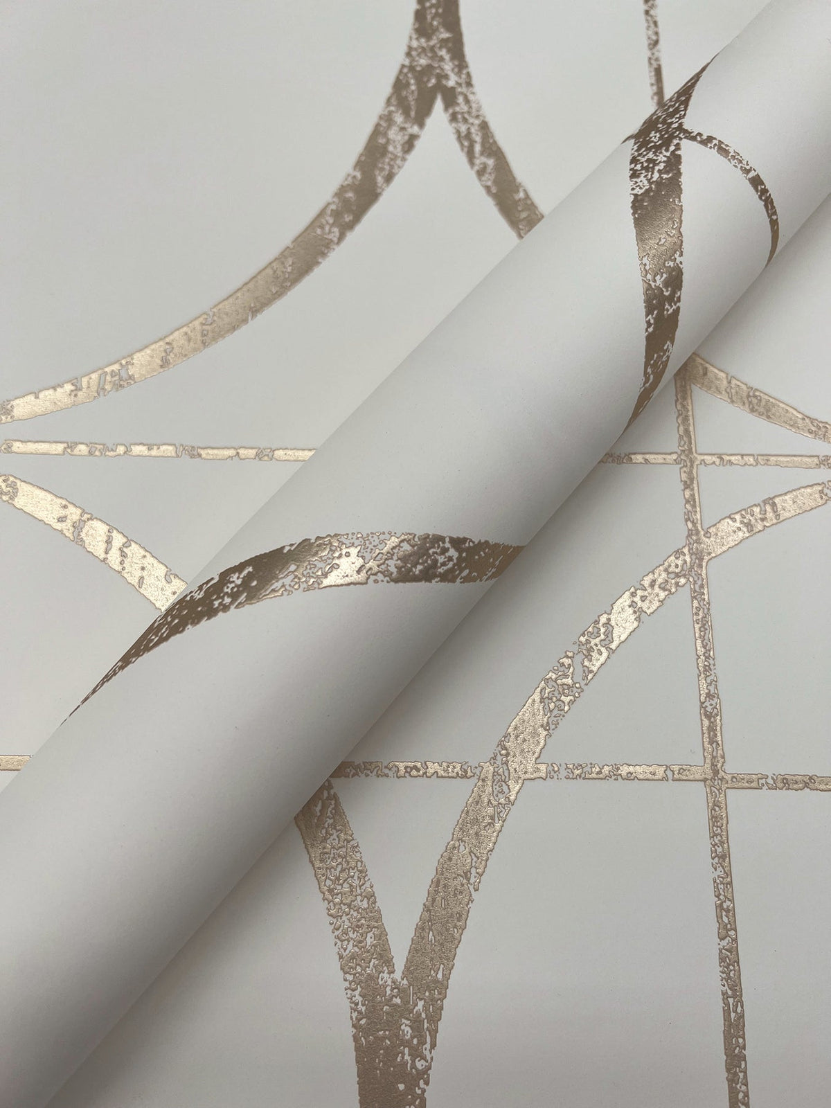 A close-up of the Sun Circles Wallpaper by York Wallcoverings, showcasing its metallic gold geometric pattern with intersecting lines and curved shapes on a crisp white background.