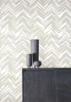 A black dresser with three matte black vases sits in front of a white wall adorned with York Wallcoverings’ Polished Chevron Wallpaper, featuring a repeating, thin black zigzag pattern.
