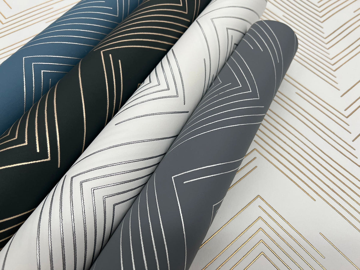 Four rolls of Polished Chevron Wallpaper by York Wallcoverings, in blue, black, white, and gray, feature metallic geometric patterns with lines forming chevrons set against a coordinating patterned background.