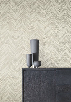 A black cabinet topped with three matte black vases stands against a cream wall adorned with York Wallcoverings’ Polished Chevron Wallpaper, featuring a subtle geometric chevron pattern in thin black lines.
