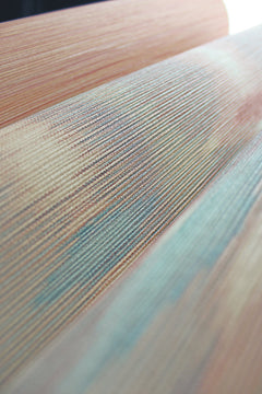 Close-up of Sunrise Flame Wallpaper by York Wallcoverings, featuring a textured surface with fine horizontal lines and a mix of peach, blue, and green hues that create an abstract, wavy design.