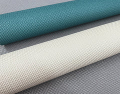 Two rolls of textured fabric—one teal, one off-white—are placed diagonally on a background featuring York Wallcoverings’ Chevronette Wallpaper in a gray zigzag pattern.