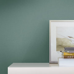 A minimalist and modern space features a green Chevronette Wallpaper by York Wallcoverings behind a white shelf displaying a framed artwork and a small stack of books, one labeled ART.