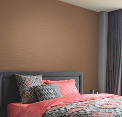 A modern bedroom featuring a padded dark gray headboard, coral pink bedding with abstract patterns, patterned pillows, and the Cannete Wallpaper by York Wallcoverings in light brown, complemented by dark floor-length curtains.