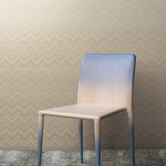 A modern chair with a gradient color from blue at the top to beige at the bottom is set against a wall covered in York Wallcoverings’ Iconic Shades Wallpaper featuring a zigzag pattern, complemented by a textured gray carpet.