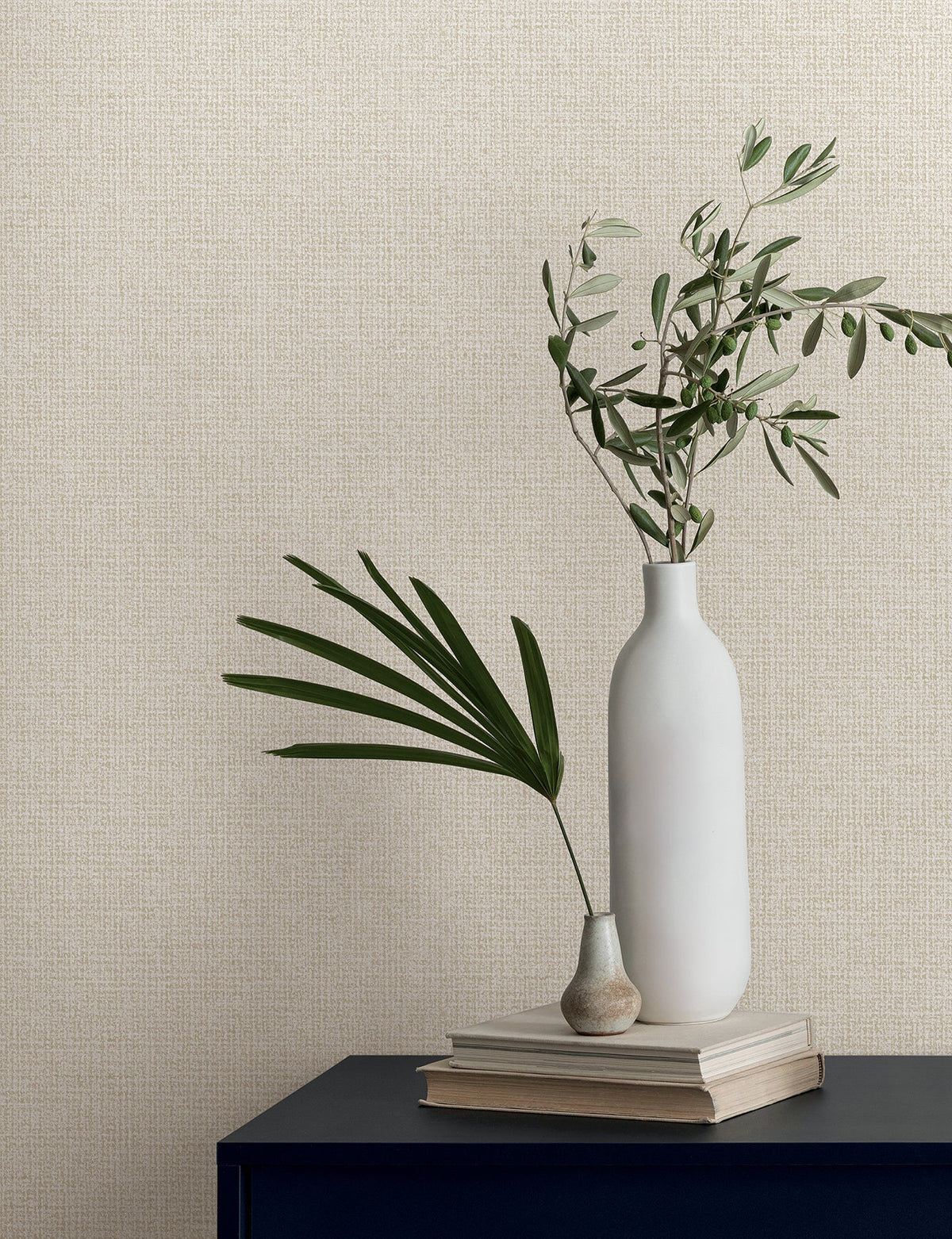 Two vases holding greenery sit on a stack of books against textured Magnolia Home Brindled Wallpaper.