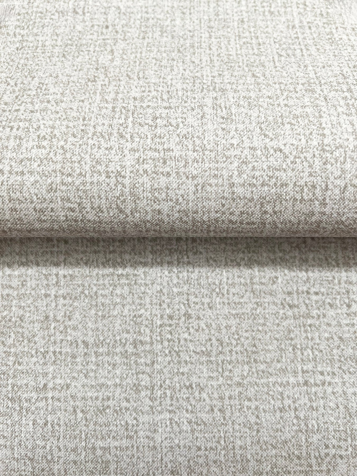 Close-up of a roll of Magnolia Home Brindled Wallpaper in tan with a mottled, textured pattern.