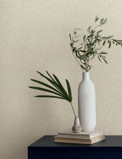 Two vases with greenery sit on a stack of books against a textured, light beige Magnolia Home Brindled Wallpaper.