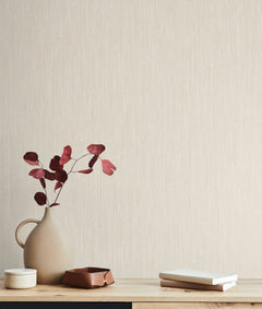 Smooth as Silk Wallpaper by York Wallcoverings in light beige with a subtle vertical texture, featuring a vase with reddish-brown leaves and small personal items on a wooden surface in the foreground.