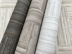 Three rolls of Tesselle Wallpaper featuring a wood-look geometric tile pattern in varying shades of gray and beige.