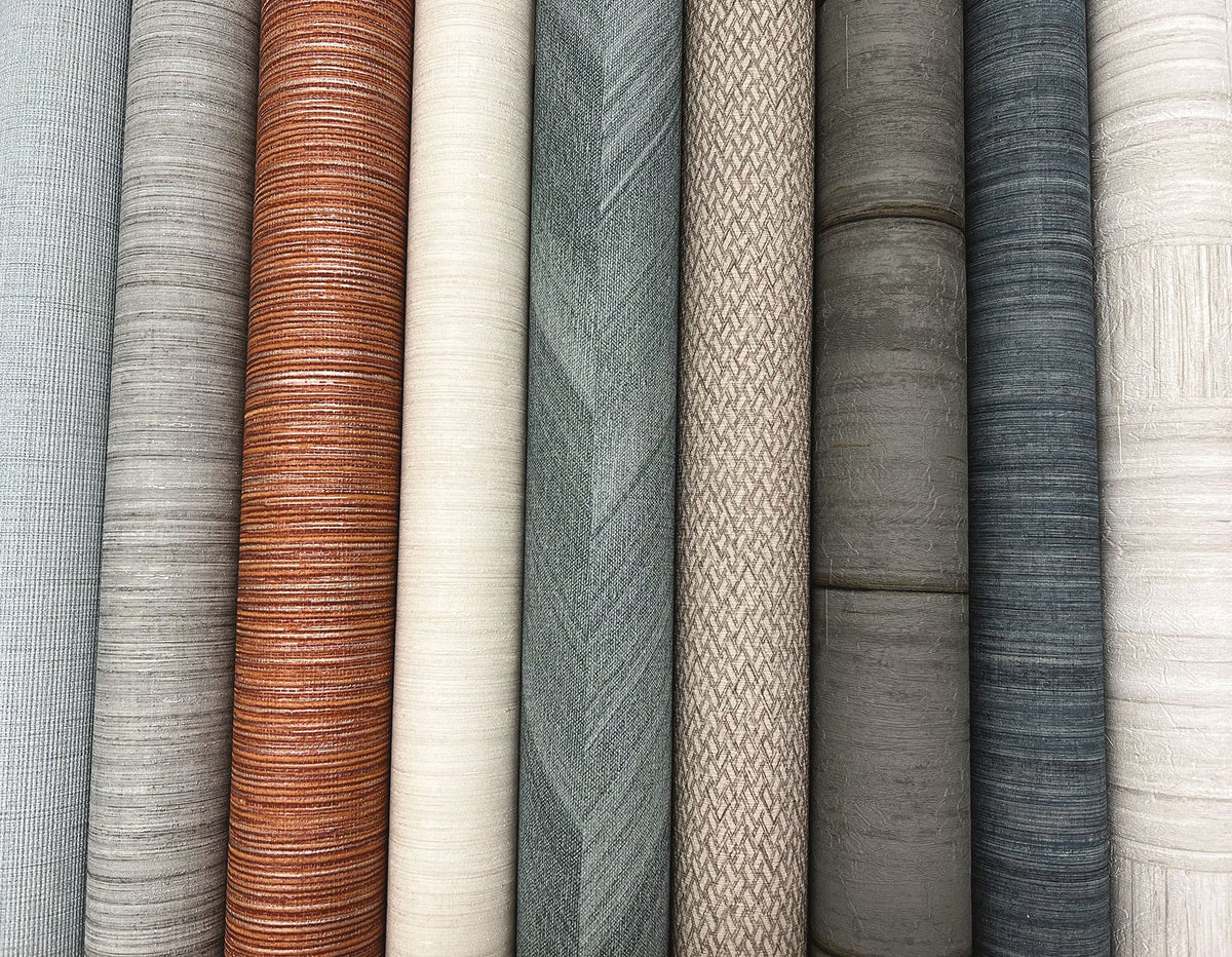 A row of Tesselle Wallpaper rolls featuring various textures and neutral color patterns.