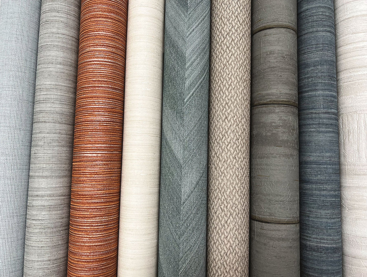 A vertical array of Tesselle Wallpaper rolls in varying shades and textures, including horizontal stripes, herringbone patterns, and solid colors.