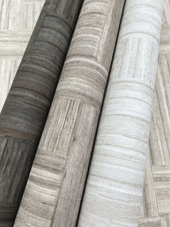 Three rolls of York Wallcoverings Tesselle Wallpaper featuring a textured, geometric wood-grain pattern in shades of dark charcoal, taupe, and light grey.