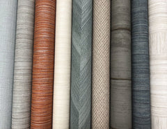 Nine rolls of Tesselle Wallpaper by York Wallcoverings displayed side-by-side in shades of grey, tan, brown, and off-white.