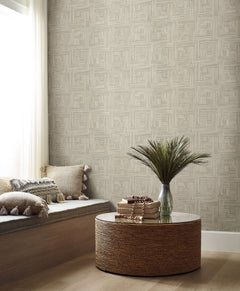 Tesselle Wallpaper featuring a geometric pattern of overlapping light brown rectangular blocks on a wall behind a seating area with a round woven table.
