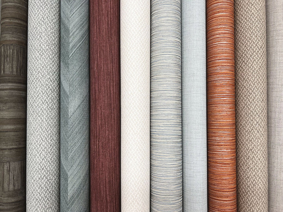 A row of Tesselle Wallpaper rolls featuring various textures and patterns in shades of gray, brown, cream, and rust.