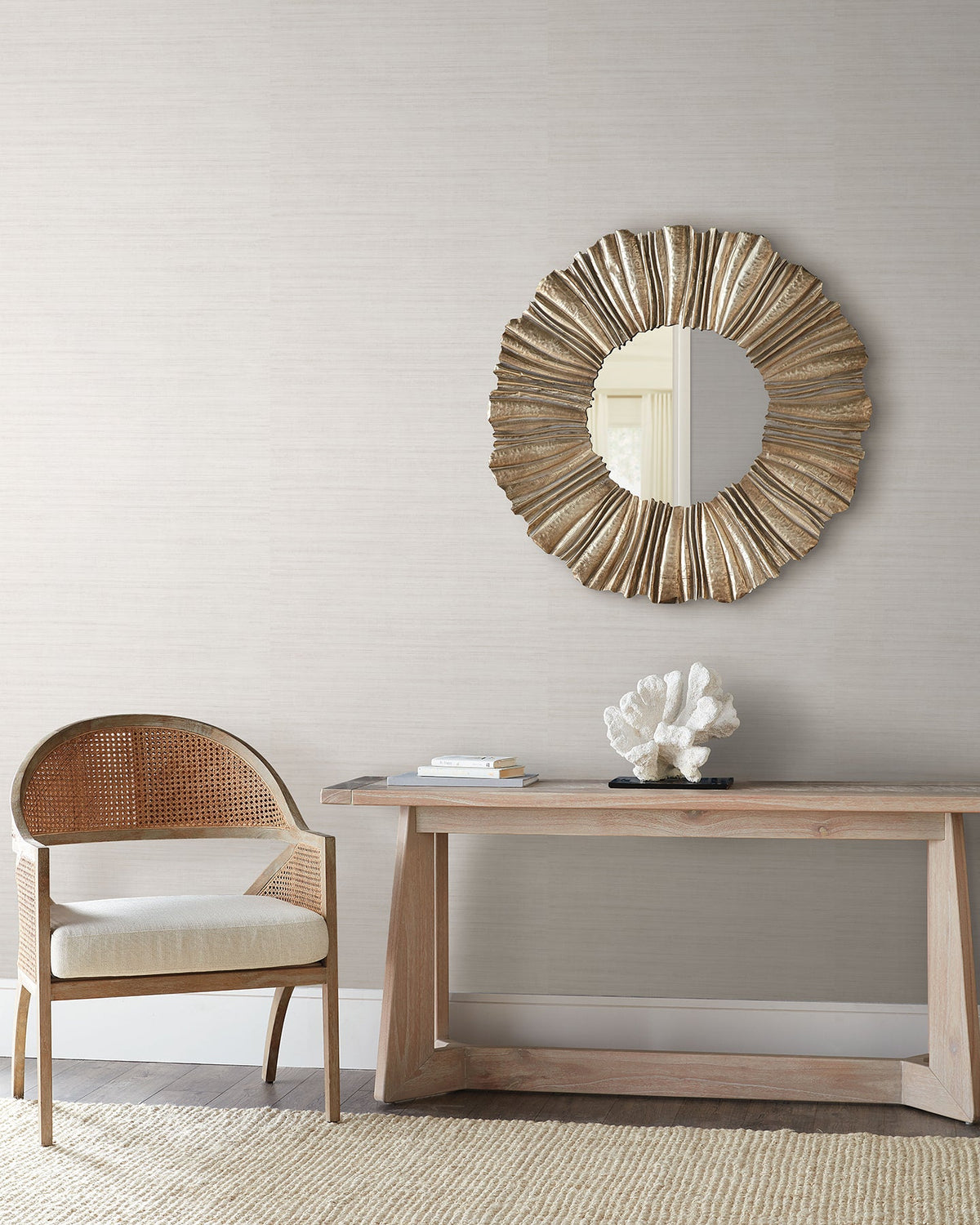 Light gray Tasar Silk Wallpaper by York Wallcoverings behind a console table with a coral sculpture and a round sunburst mirror.