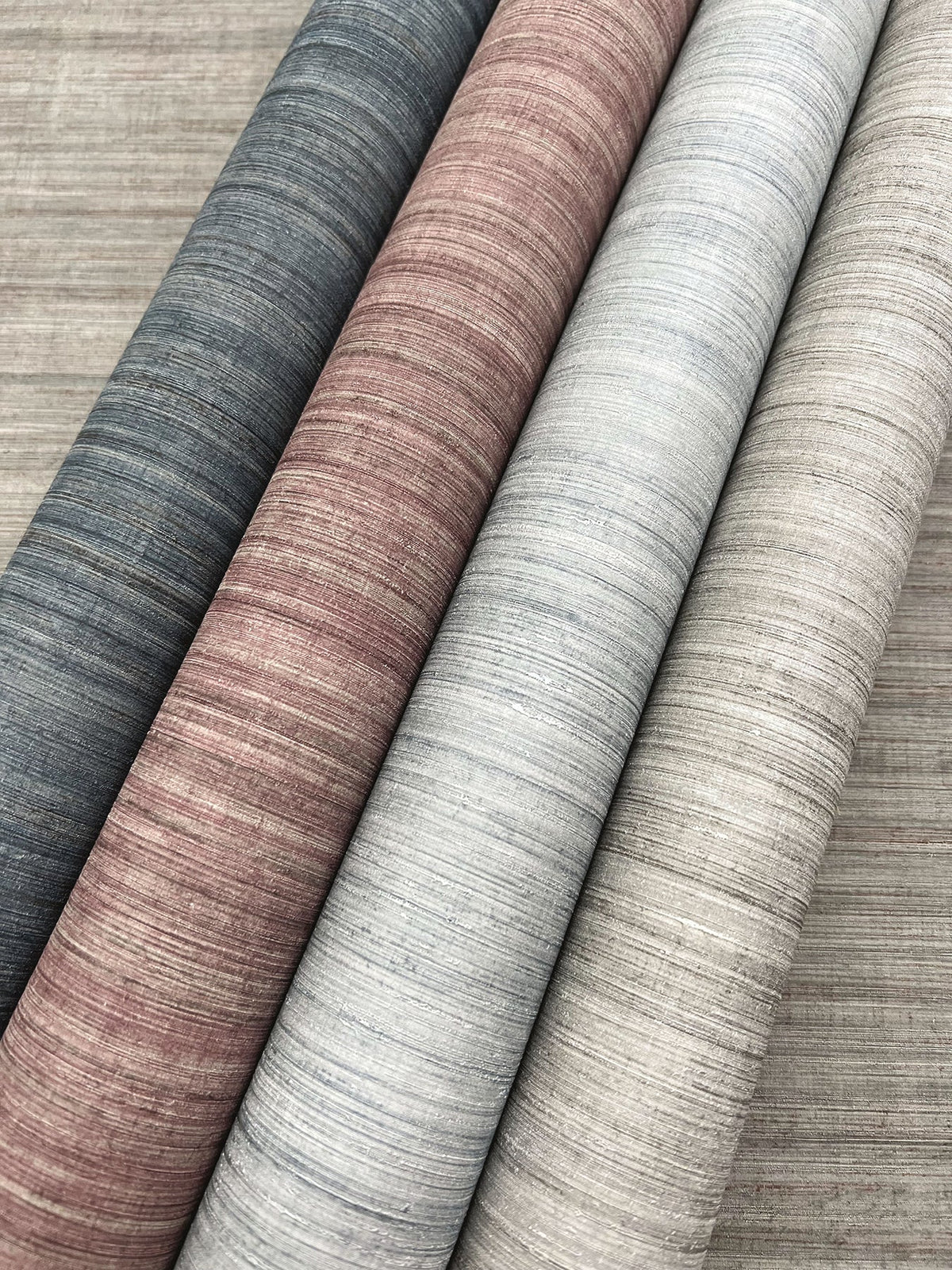 Four rolls of Tasar Silk Wallpaper in shades of gray, mauve, light blue, and beige displayed side-by-side.