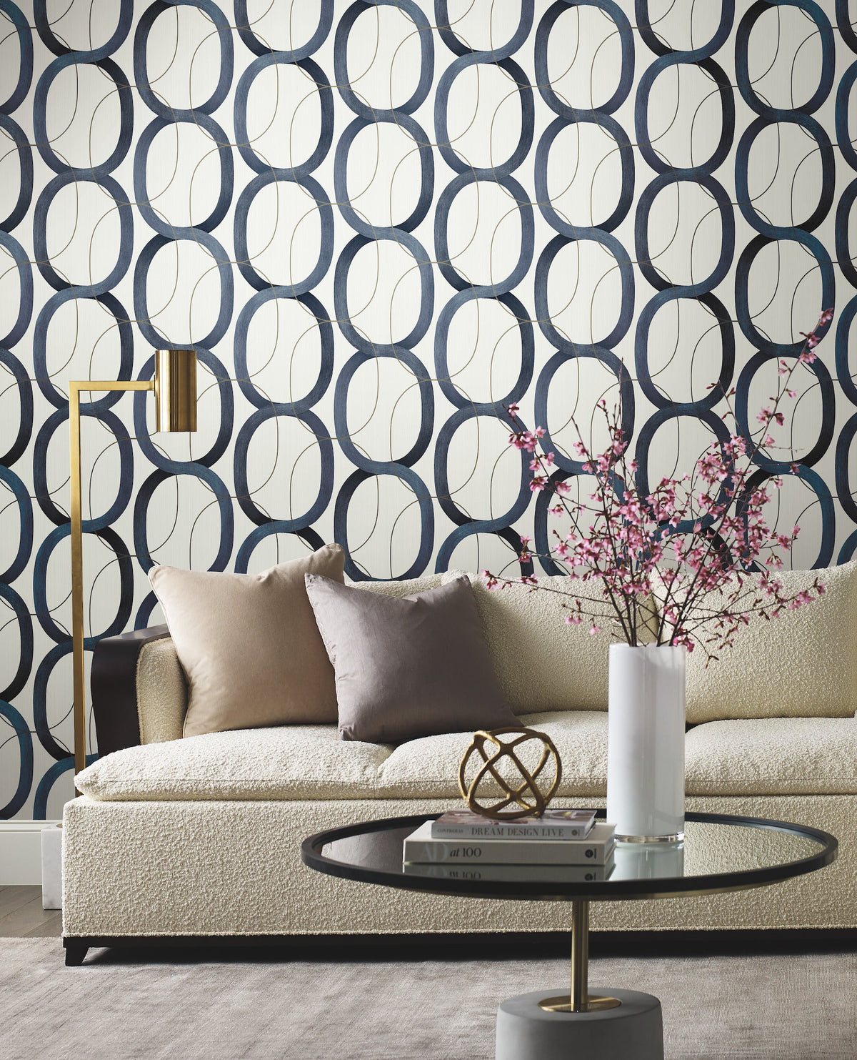 Candice Olson Interlock Wallpaper featuring a repeating pattern of interlocking dark blue and gold-outlined oval rings on a white background, behind a sofa and coffee table.