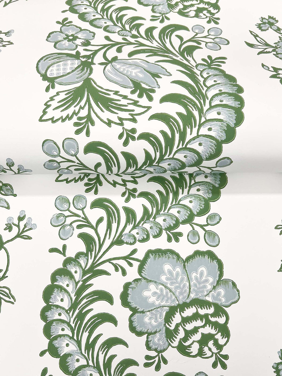 The Beaumont Floral Stripe Wallpaper by York Wallcoverings features a white background adorned with a repeating pattern of green and light blue floral and leafy designs, including large flowers and winding leafy vines.