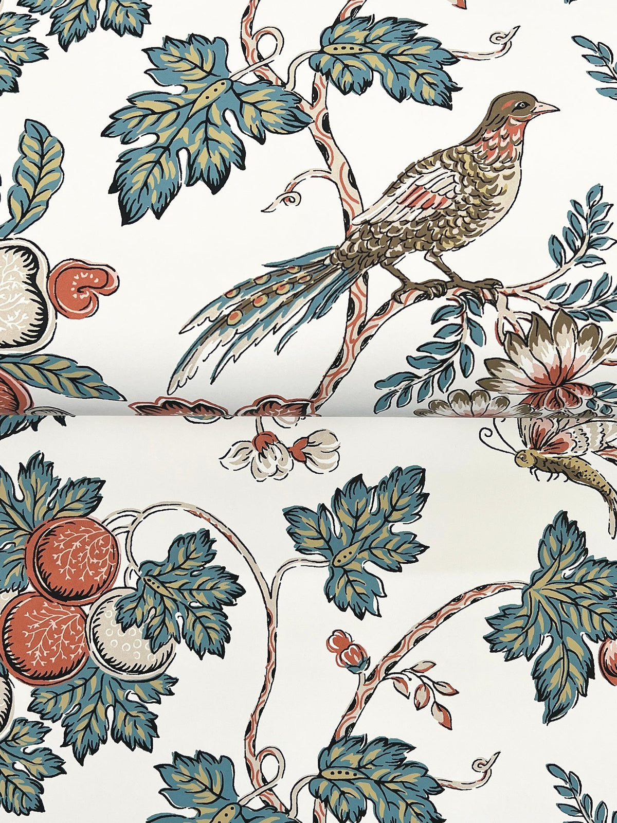 The Parterre Jacobean Wallpaper by York Wallcoverings features a bird perched on a branch, surrounded by large leaves, flowers, and round fruit shapes in muted green, red, and blue tones on a white background.
