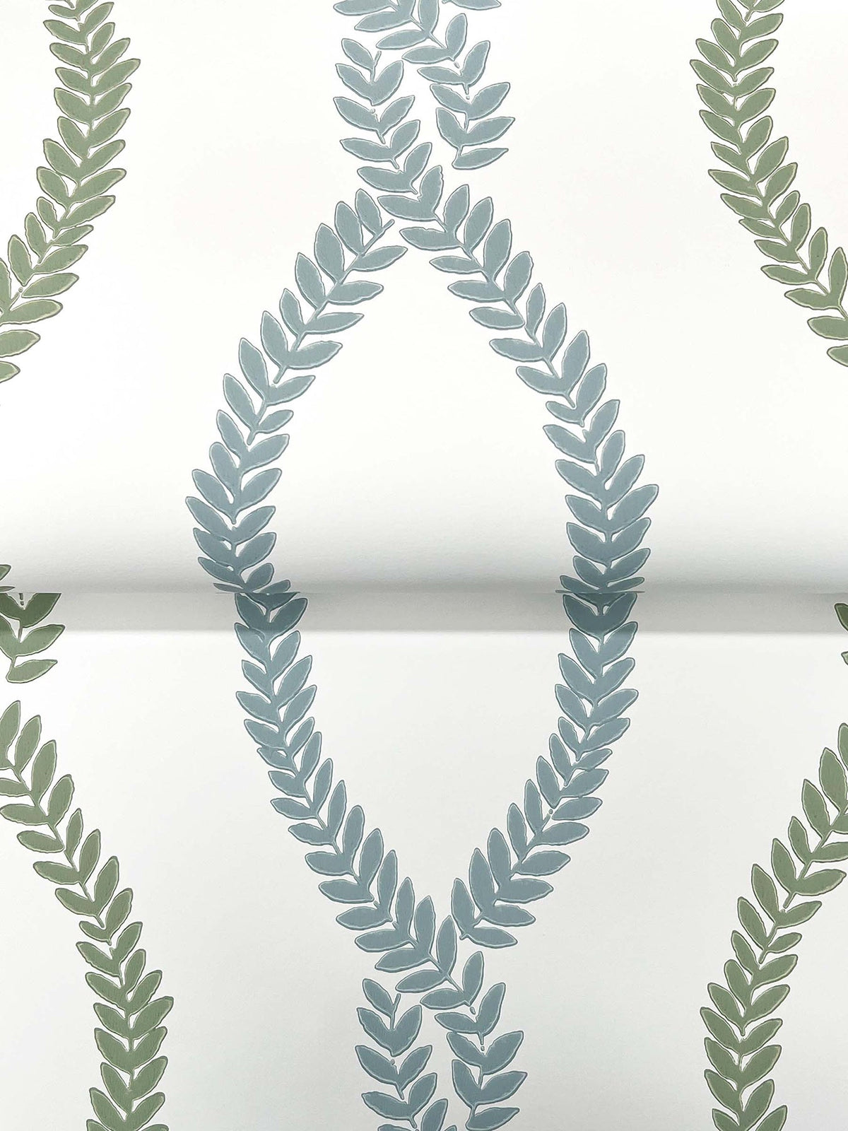 York Wallcoverings’ Laureate Vine Trellis Wallpaper features a repeating pattern of green and blue leafy vines forming oval and curved shapes on a white background.