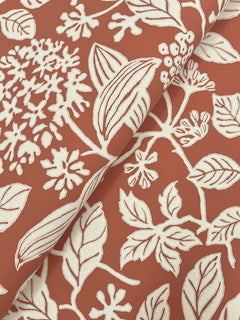 Rowen Botanical Wallpaper by York Wallcoverings showcases cream-colored botanical patterns of leaves, berries, and flowers set against a terracotta background.