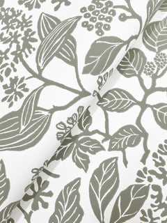 Rowen Botanical Wallpaper by York Wallcoverings showcases a hand-drawn botanical pattern in gray on a white background, featuring an elegant array of leaves, branches, and flowers. The wallpaper is slightly folded in the image, revealing a subtle diagonal crease across its surface.