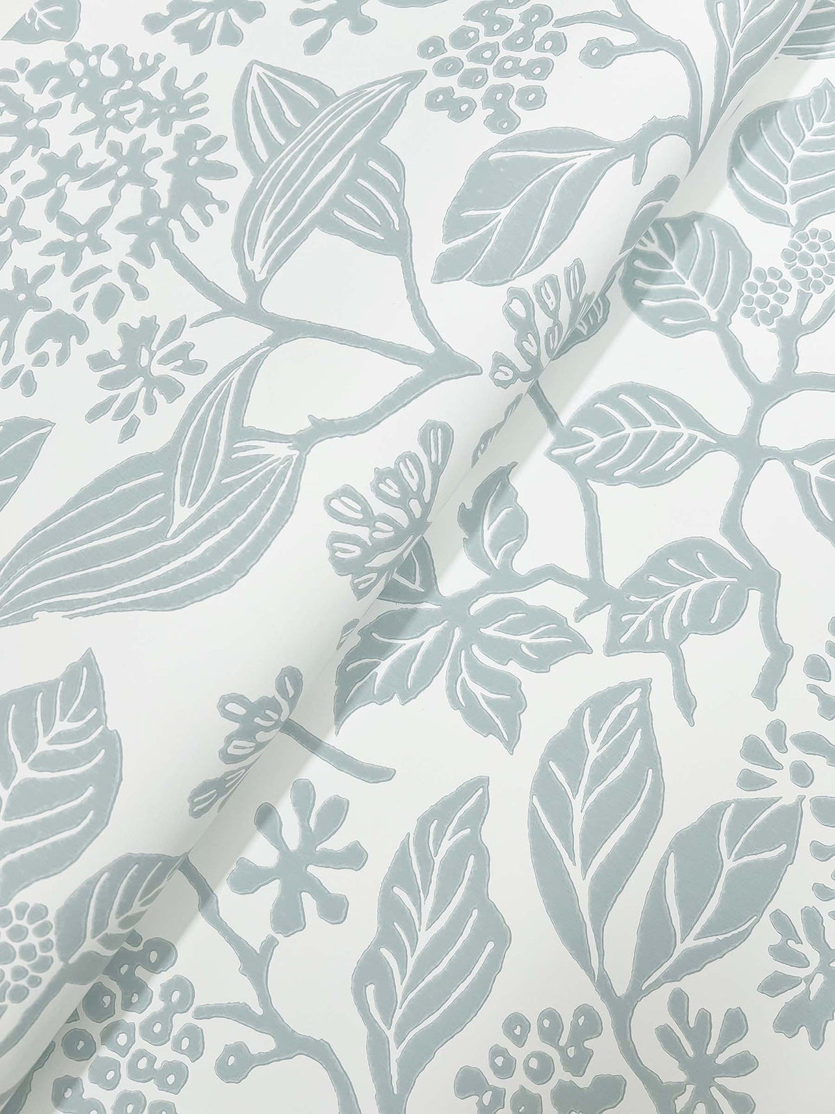 Close-up of Rowen Botanical Wallpaper by York Wallcoverings, showcasing a white background with a light gray botanical pattern of leaves, branches, and berries; the wallpaper is partially folded, creating shadows that accentuate its textured surface.