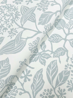 Close-up of Rowen Botanical Wallpaper by York Wallcoverings, showcasing a white background with a light gray botanical pattern of leaves, branches, and berries; the wallpaper is partially folded, creating shadows that accentuate its textured surface.
