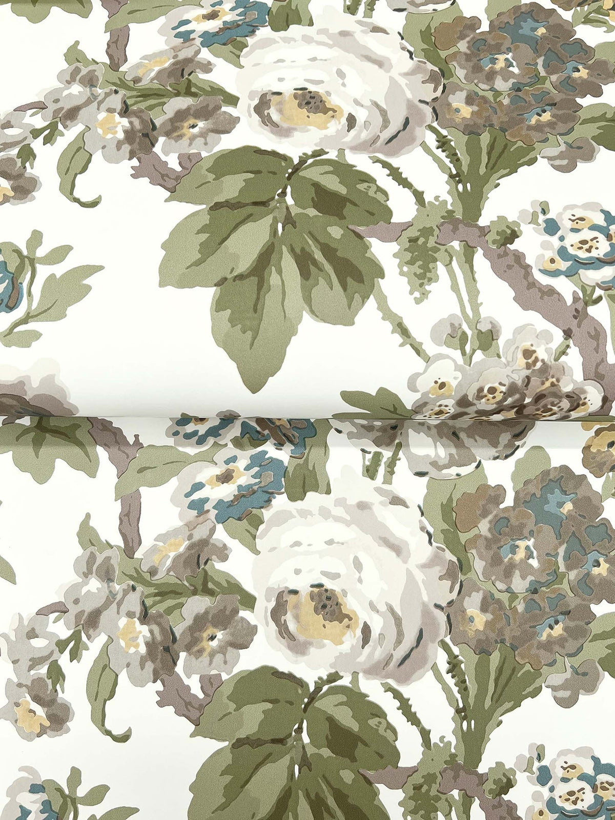 The Beatrix Vintage Floral Wallpaper by York Wallcoverings showcases a graceful floral pattern with large white roses, green leaves, and blue accents on a crisp white background. The design also features a subtle fold near the center.