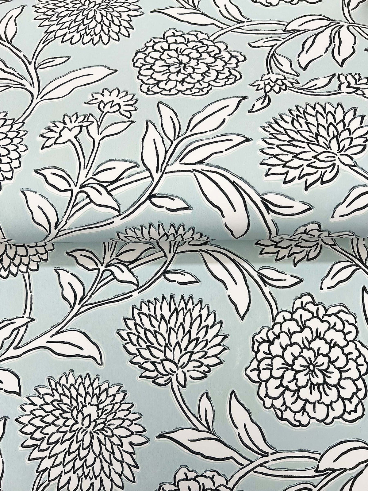 Chatsworth Garden Floral Trail Wallpaper by York Wallcoverings features a light blue background adorned with a black and white floral pattern of large, detailed flowers and leafy stems. The design is shown on gently folded wallpaper.