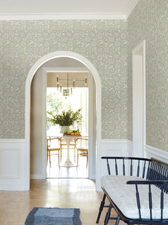 A bright hallway featuring Chatsworth Garden Floral Trail Wallpaper by York Wallcoverings, a black bench with a cushion, an arched doorway, and a view into a dining area with a round white table, wooden chairs, and a vase of greenery.