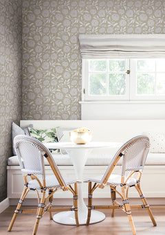 Bright, cozy breakfast nook with a round white table, two woven chairs, a built-in bench with cushions, and a window with white Roman shades letting in light. The space features Chatsworth Garden Floral Trail Wallpaper by York Wallcoverings.