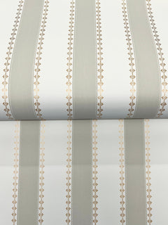 A close-up of York Wallcoverings’ Tilford Awning Stripe Wallpaper shows alternating wide beige and narrow white vertical stripes, each edged with small gold geometric patterns. The roll introduces a subtle horizontal break in the design.