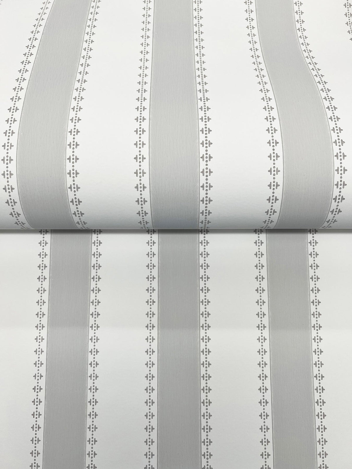 A close-up of the Tilford Awning Stripe Wallpaper by York Wallcoverings, featuring vertical gray and white stripes bordered by small, repeating diamond and dot patterns. The wallpaper is shown partially unrolled on a flat surface.