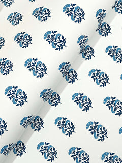 The Sylvie Floral Wallpaper by York Wallcoverings features a white surface adorned with a repeating pattern of dark blue leaves and light blue flowers, uniformly arranged across the material. A diagonal crease is visible in the image.